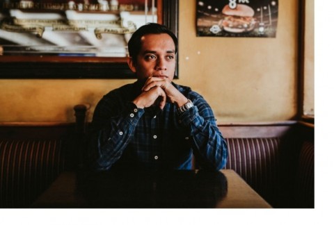 Person sitting at cafe table looking thoughtful chin resting on their hands