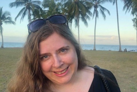 Bron on the beach with palm trees and the ocean behind her