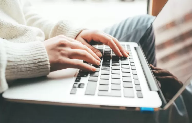 Person wearing a light coloured woolen jumper working on a Macbook Air